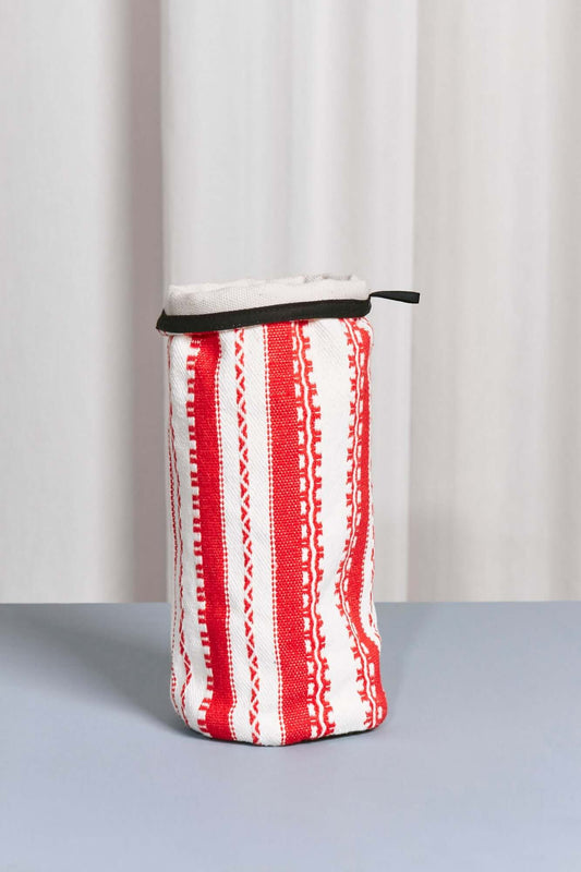 Funda cilíndrica de tela blanca y roja con rayas verticales y cenefas, borde superior negro y diseño textil artesanal.