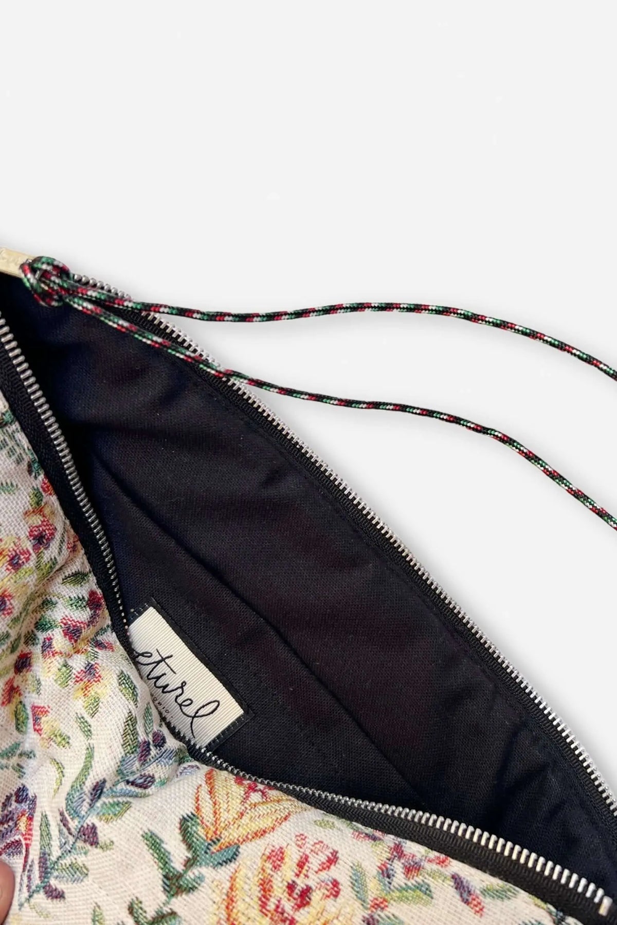 Computer sleeve in cream jacquard fabric with a colorful azalea floral pattern and black lining, featuring a zipper.