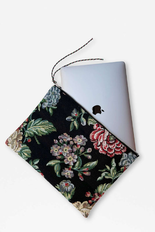 Laptop sleeve in black floral jacquard fabric featuring colorful peonies, with a zipper closure and pull cord.
