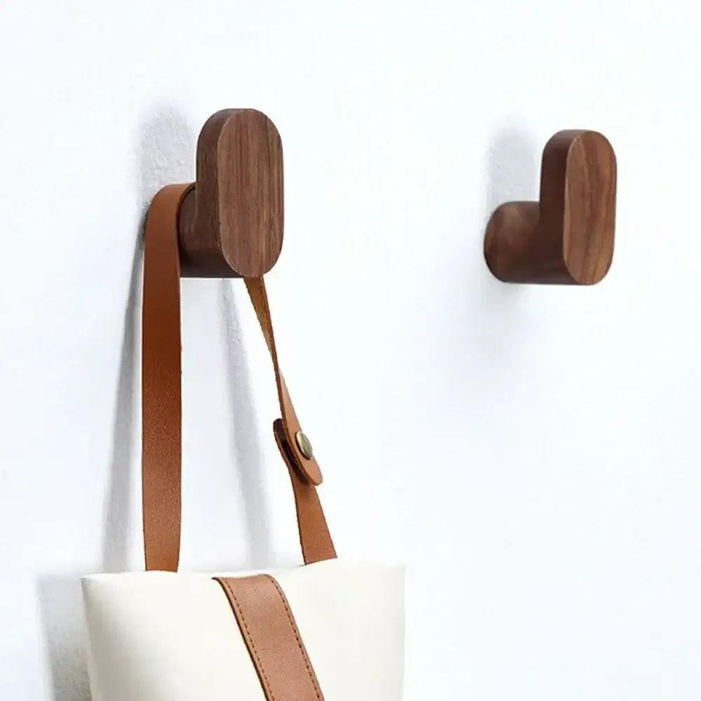 Dos perchas de pared minimalistas en madera maciza oscura, una con un bolso colgado, sobre un fondo blanco.