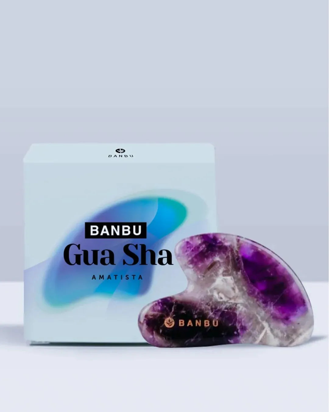 Gua Sha de amatista natural con vetas blancas junto a su caja de cartón de la marca Banbu sobre fondo claro.