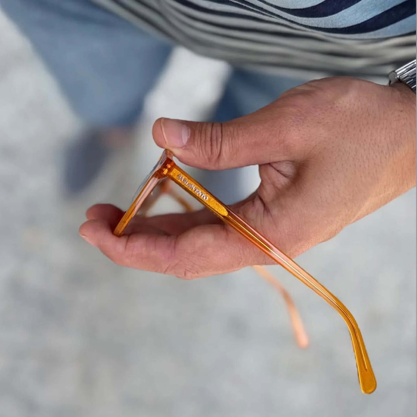 Gafas de sol de acetato transparente color naranja brillante, sostenidas en mano, estilo moderno y traslúcido.