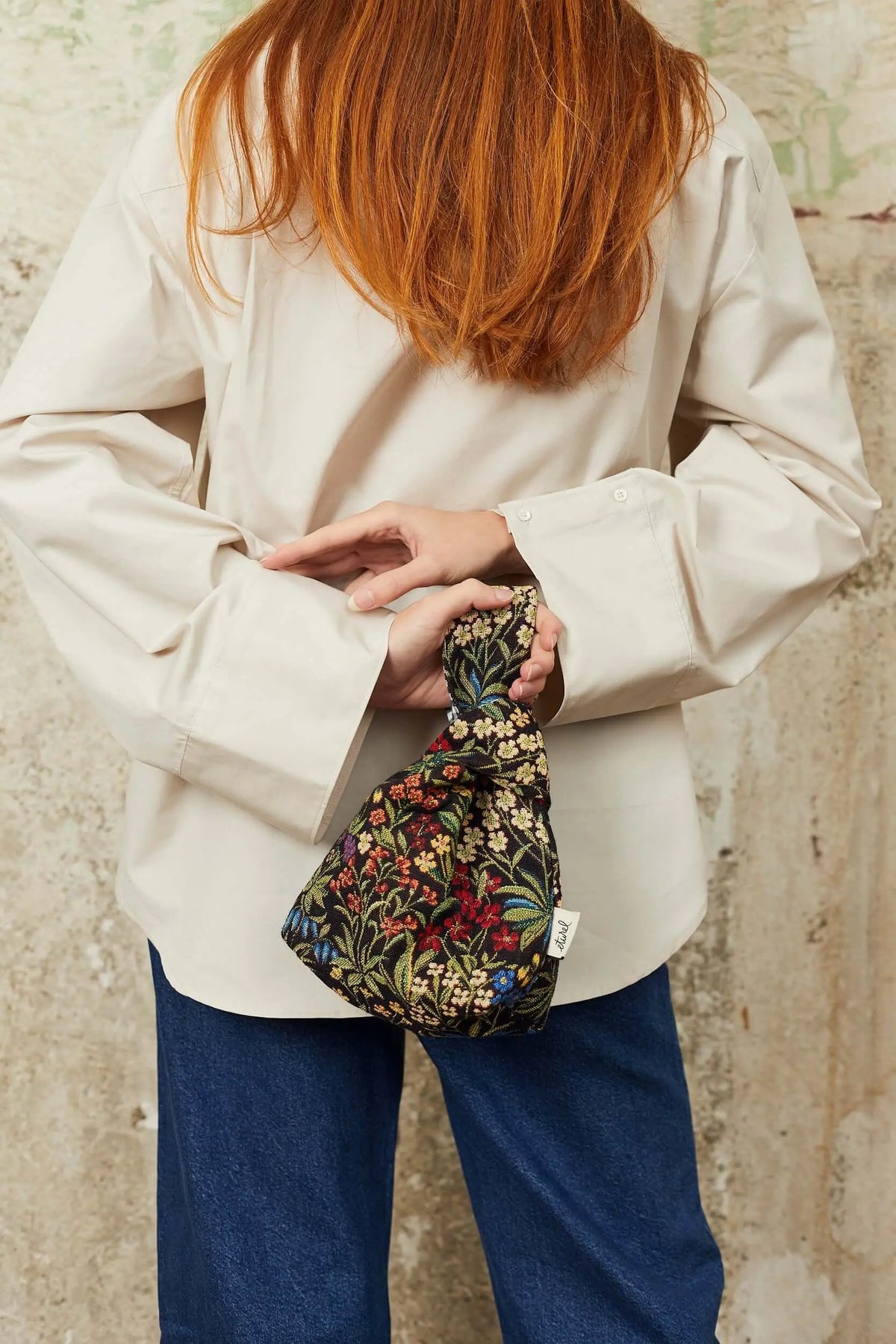 Mini knotted handbag in black jacquard fabric with a colorful floral daisy pattern, held behind a person's back.