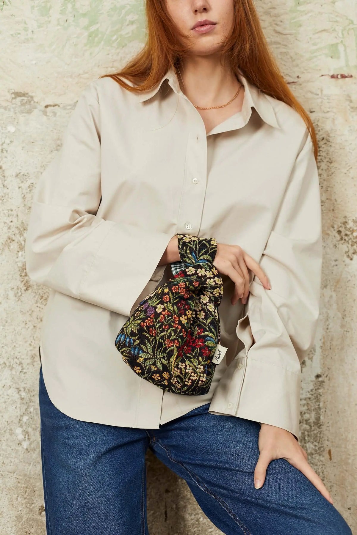 Mini hatillo bag in black jacquard fabric with a colorful floral and daisy print, held by a knotted top handle.