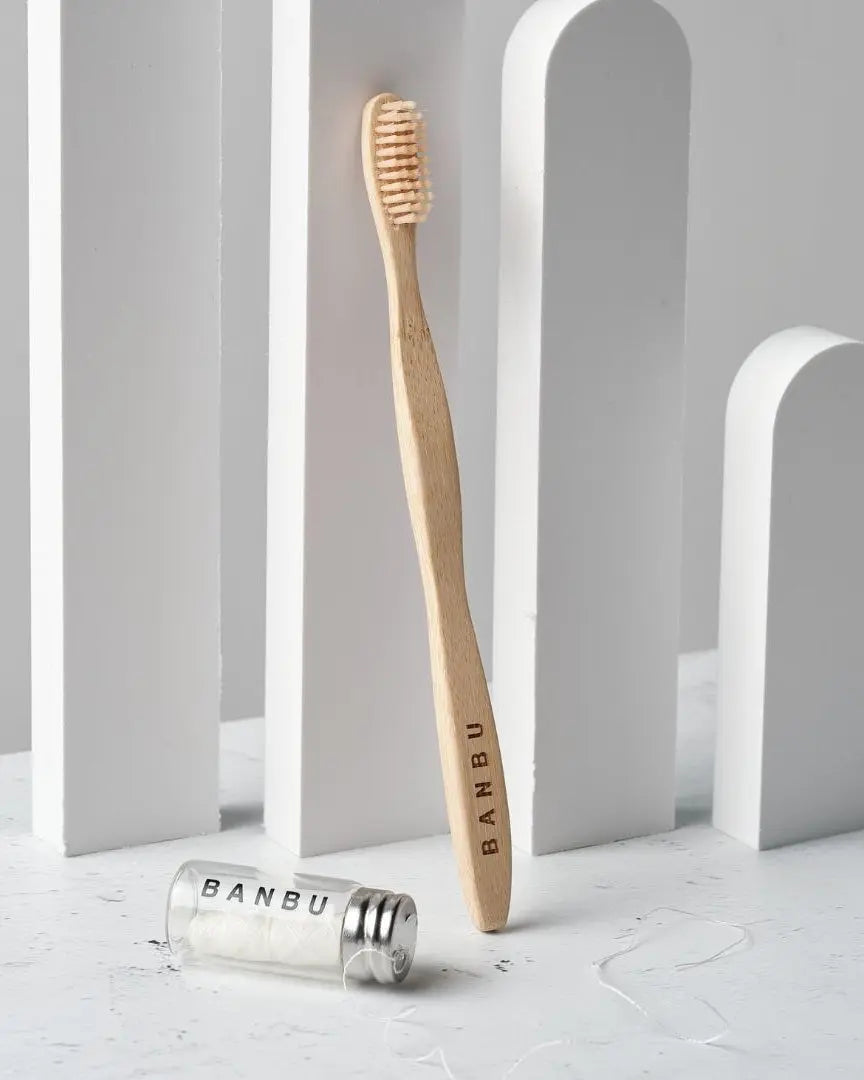 Cepillo de bambú Banbu y dispensador de hilo dental vegano de cristal sobre fondo minimalista blanco.