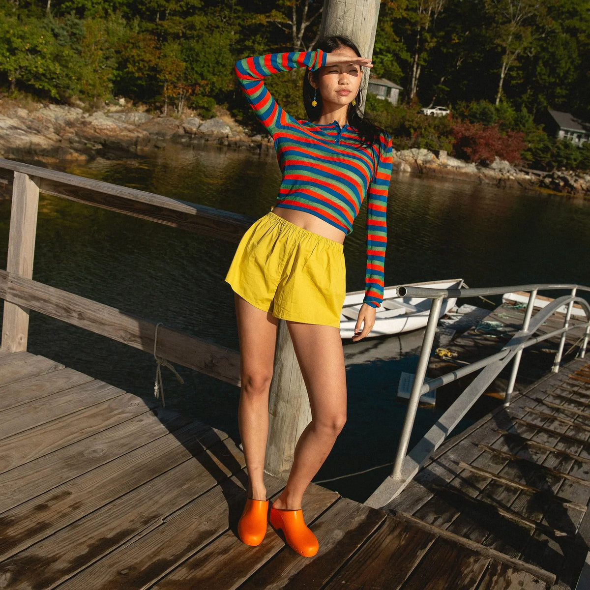 Bright orange rubber clogs, slip-on style with a smooth, hole-free rounded toe design on a wooden dock.