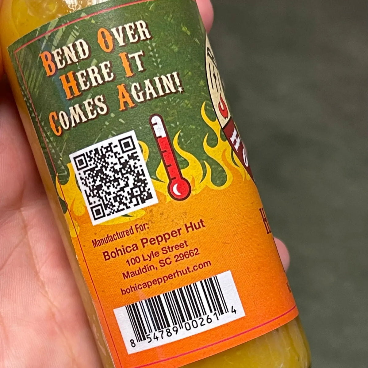 A bottle of Hawaiian Lava hot sauce with a yellow sauce, orange label, QR code, and thermometer graphic.