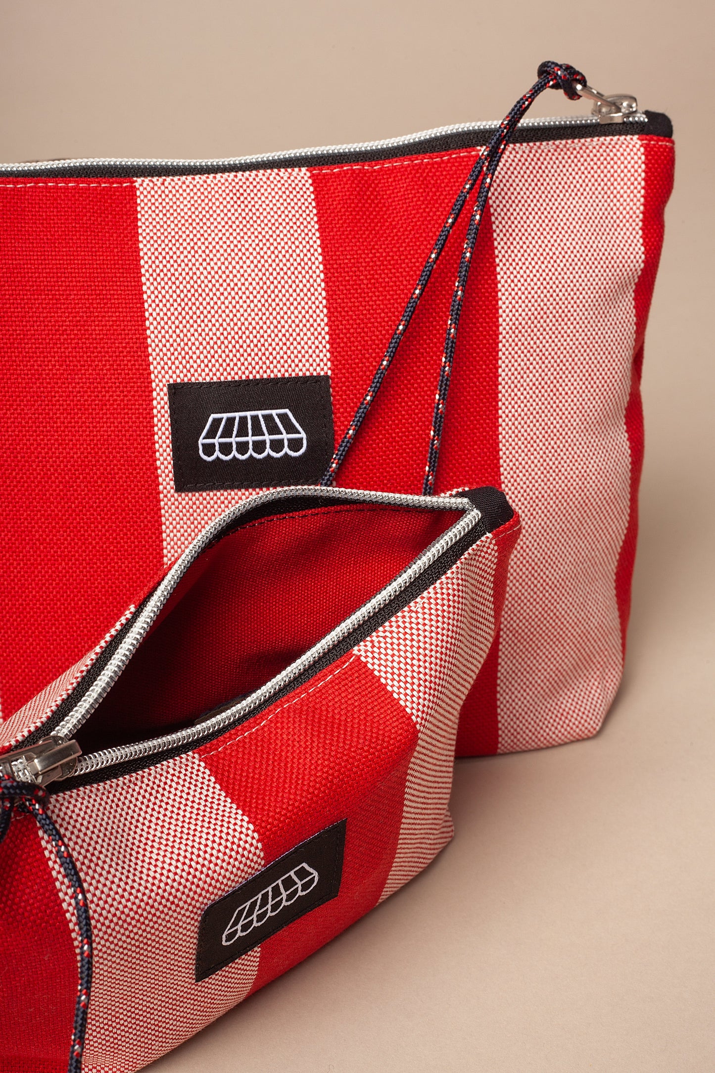 Two red and white striped canvas toiletry bags with zipper closures, rope wrist straps, and a small awning logo patch.