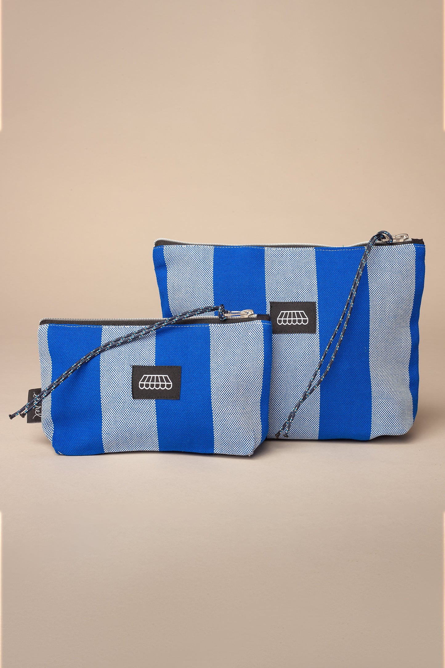 Two blue and white striped canvas zippered pouches with matching cord wrist straps on a plain beige background.