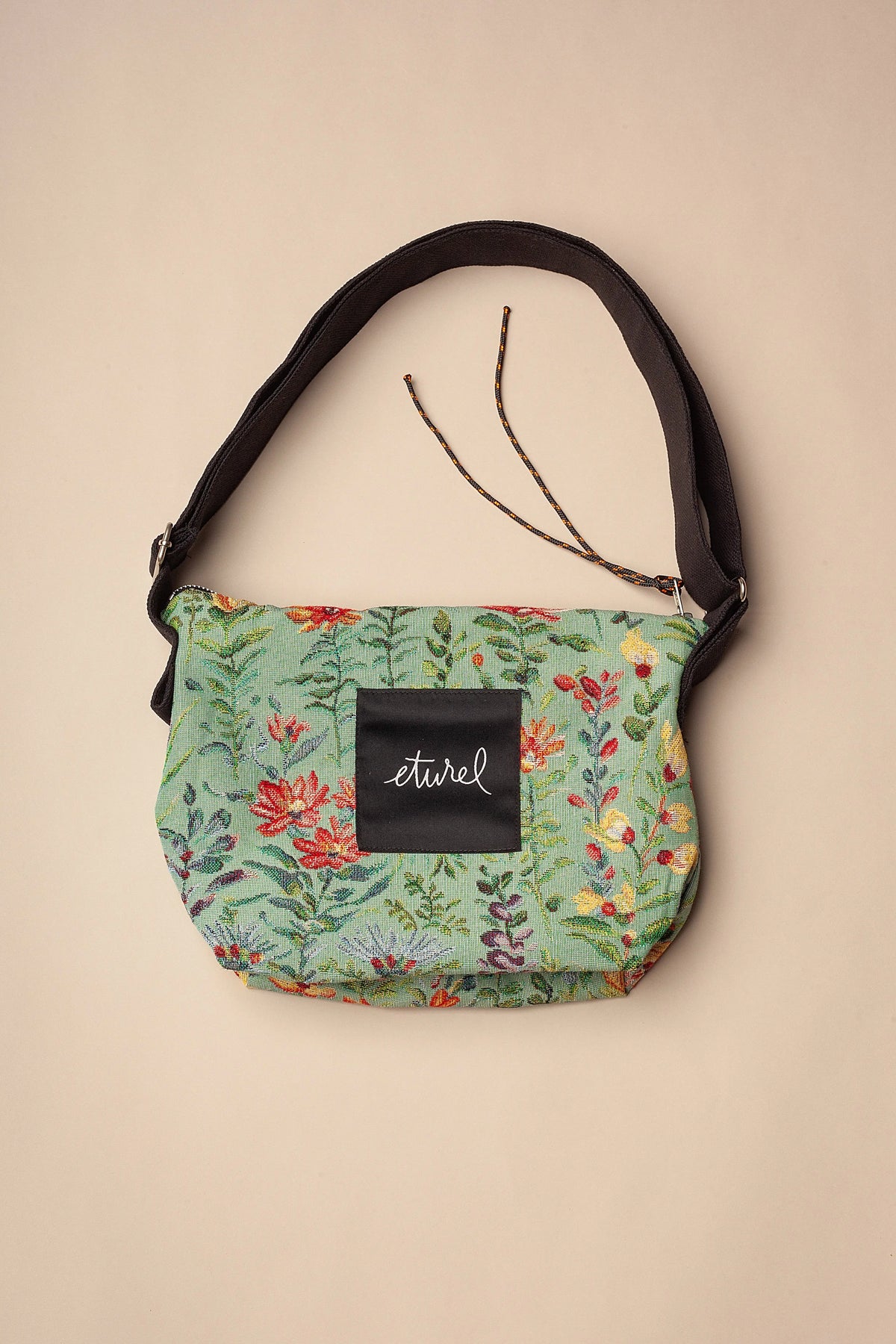 Bolso bandolera de jacquard celeste con estampado de flores coloridas, correa negra ajustable y cierre de cremallera.