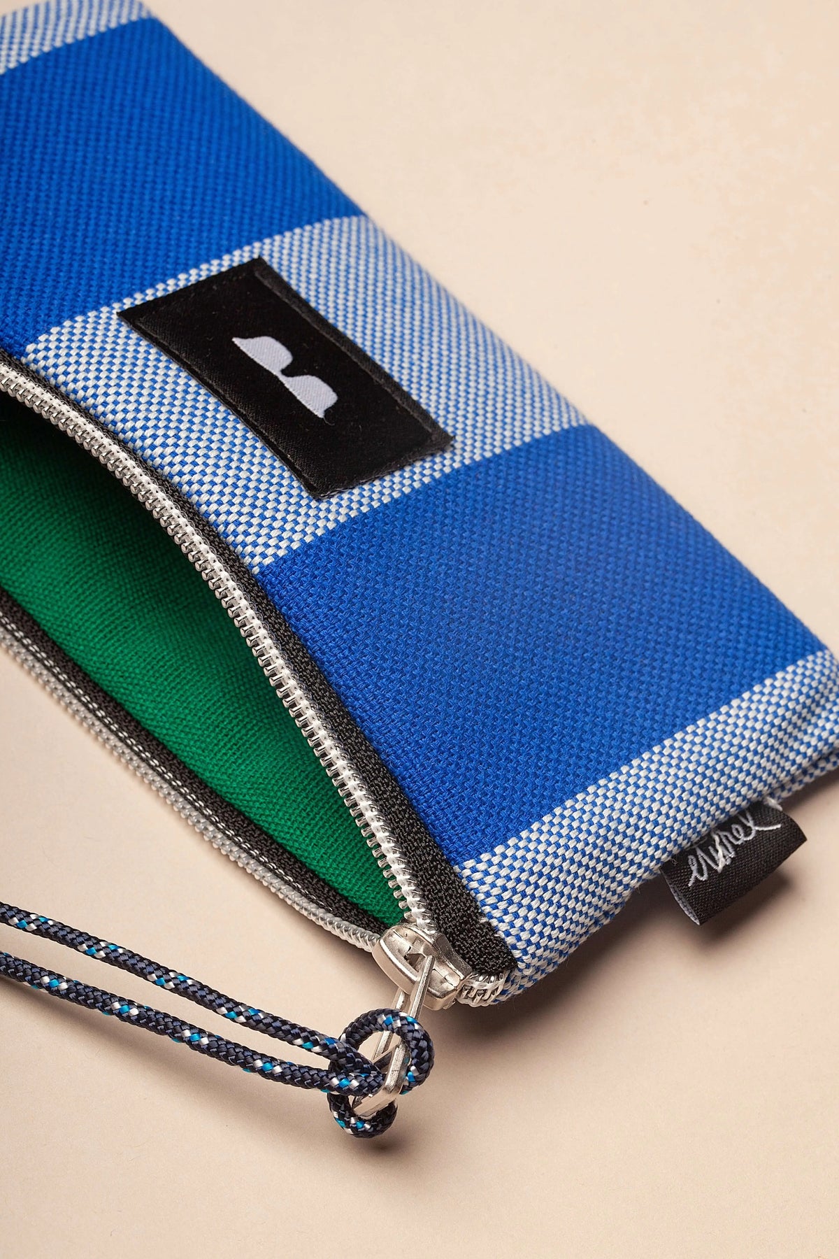 Funda para gafas de lona azul y blanca, con cremallera, interior verde y cordón decorativo estampado.