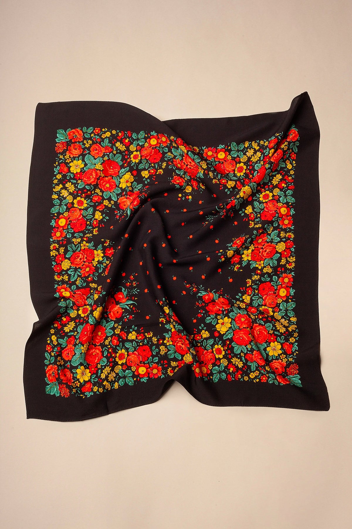 Black square headscarf featuring a vibrant floral print with red roses, yellow flowers, and green leaves.