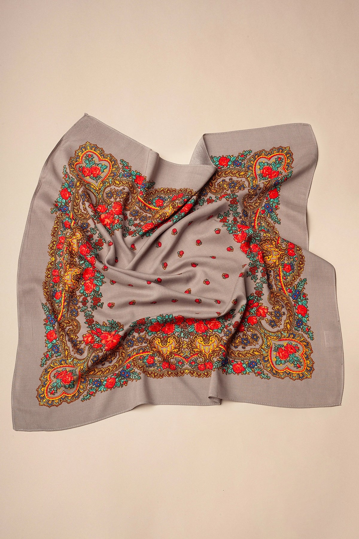 Grey square scarf with vibrant floral chain patterns in red, yellow, and blue, featuring a soft, folded fabric look.