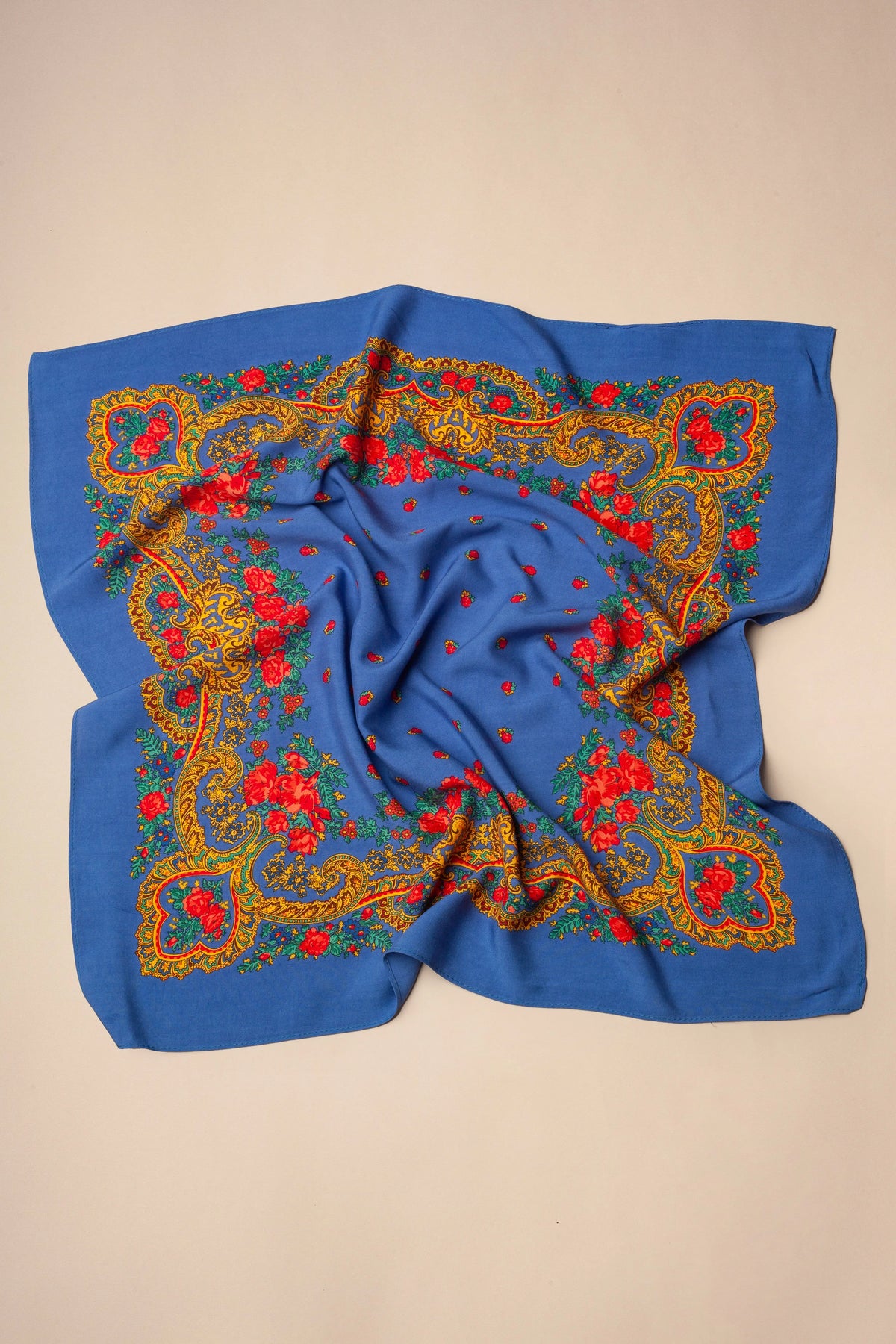 Pañuelo azul con estampado tradicional de flores rojas y bordes ornamentados en tonos dorados sobre fondo beige.