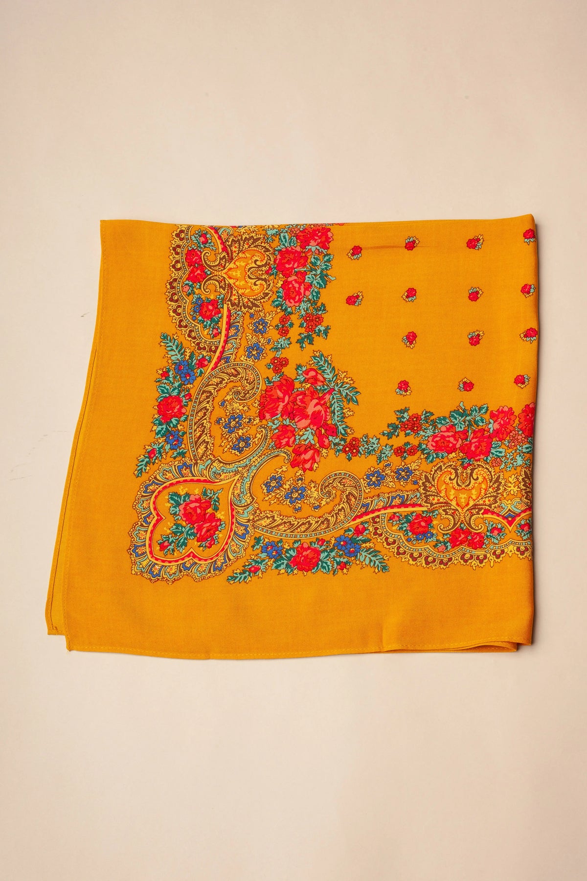 Pañuelo ocre con estampado floral tradicional, bordes ornamentados con motivos de cadenas y detalles en rojo y azul.