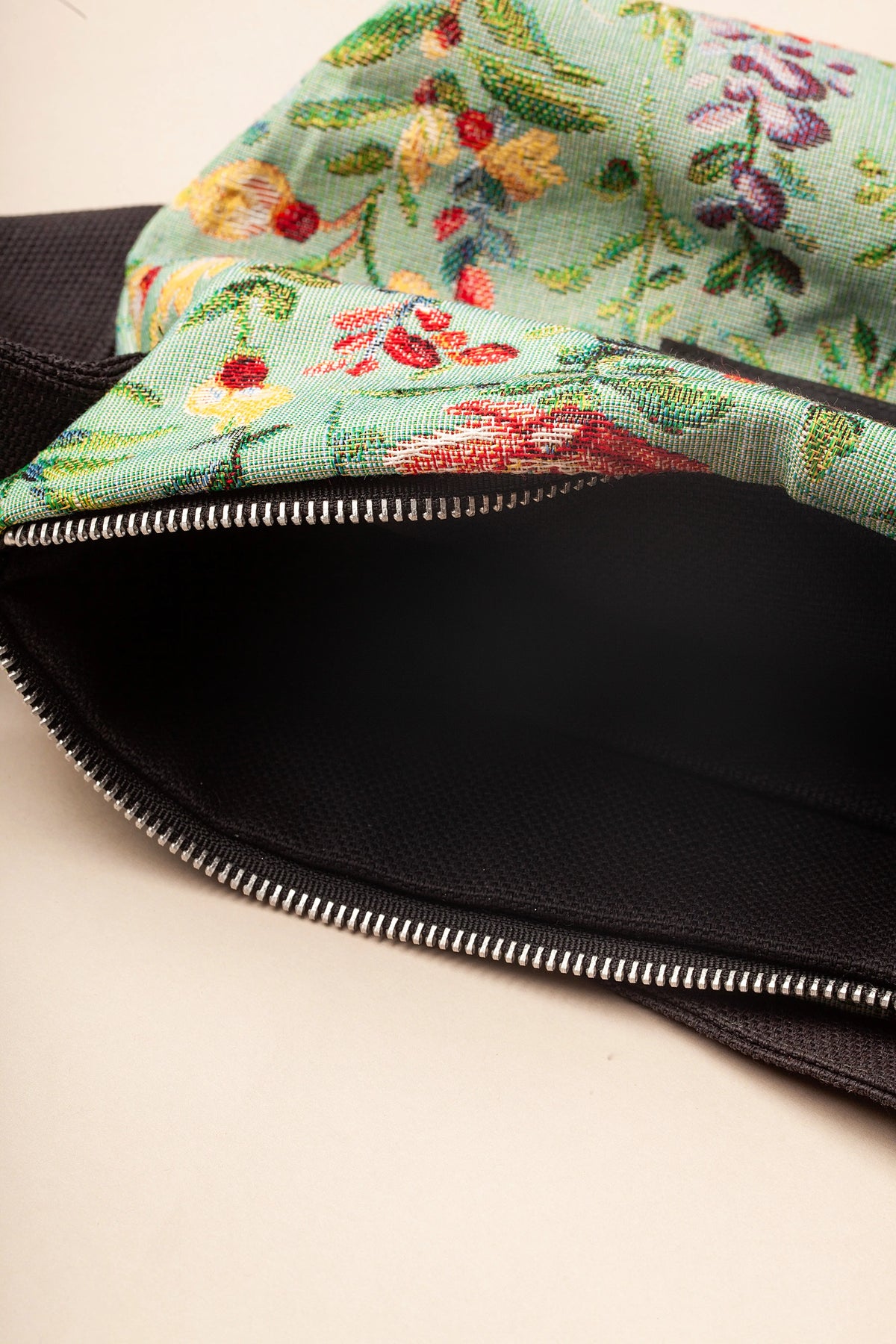 Bolso bandolera de tejido jacquard celeste con estampado de azaleas coloridas, cierre de cremallera y detalles negros.