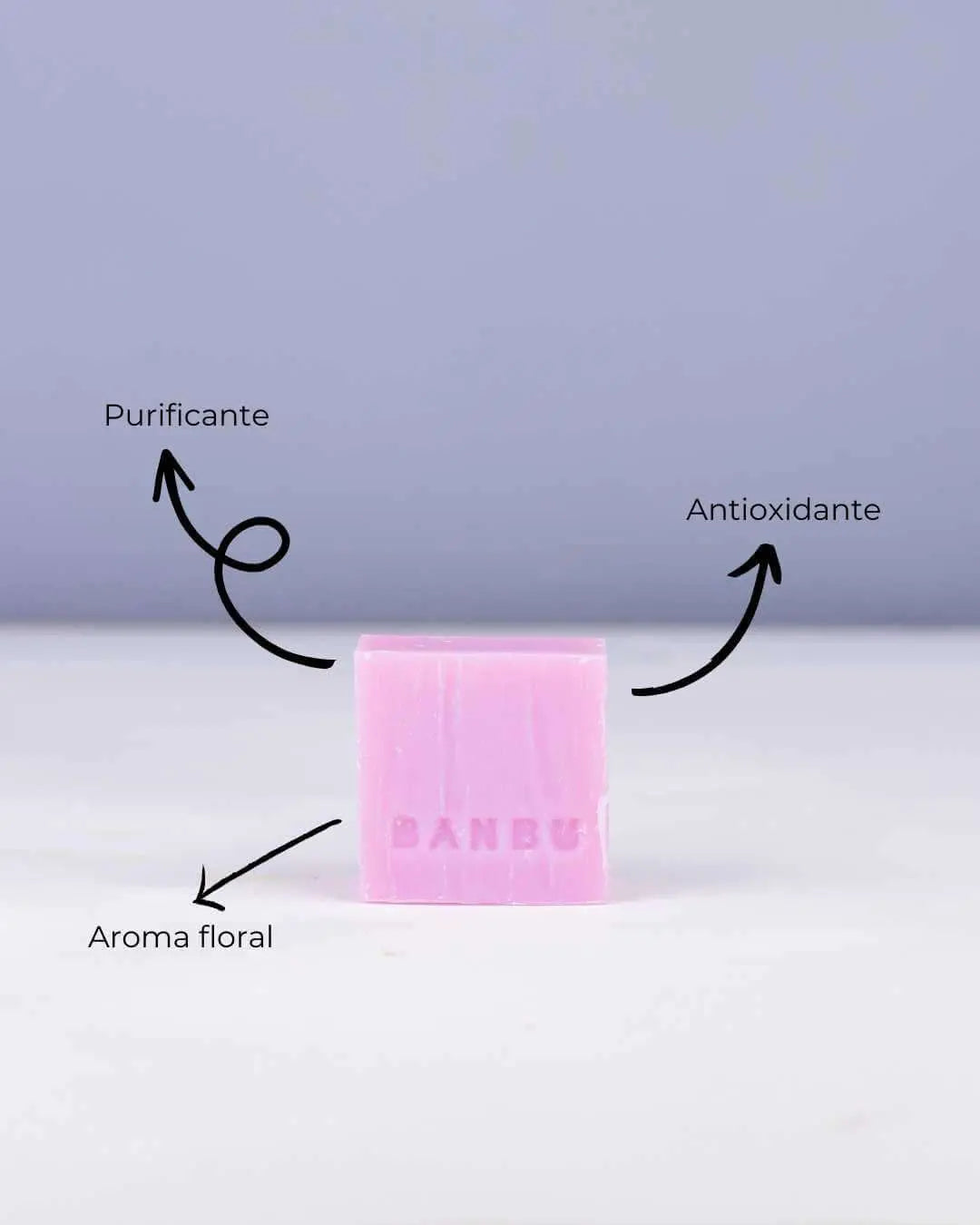 Jabón sólido rosa de Banbu con textura natural sobre fondo lila. Indica propiedades purificantes, antioxidantes y aroma.