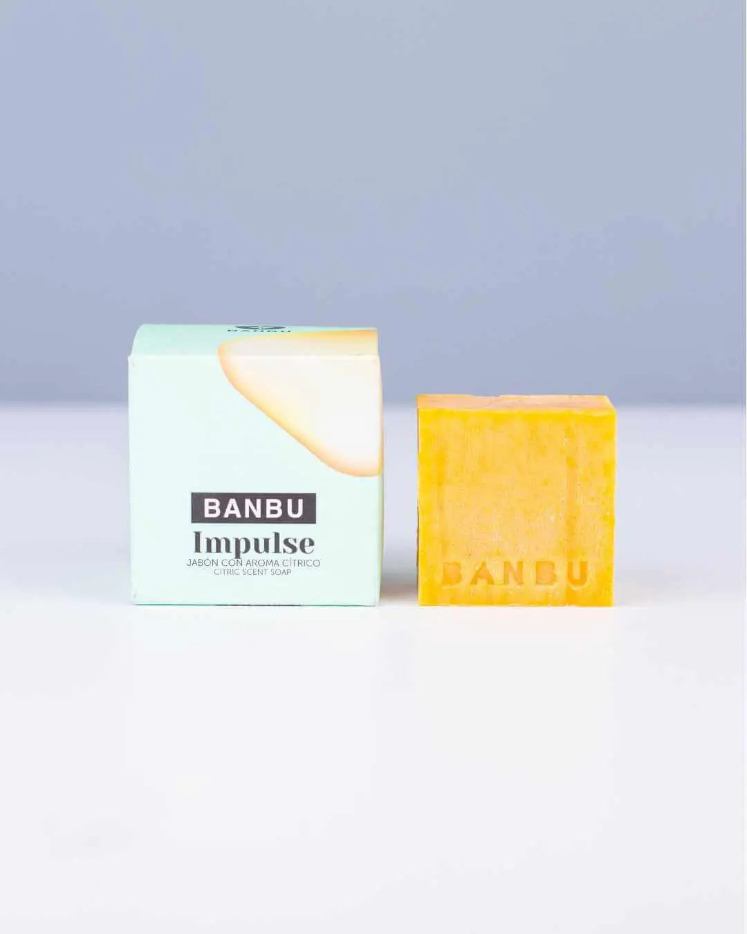 Jabón sólido naranja Banbu Impulse junto a su caja de cartón verde claro sobre fondo gris.