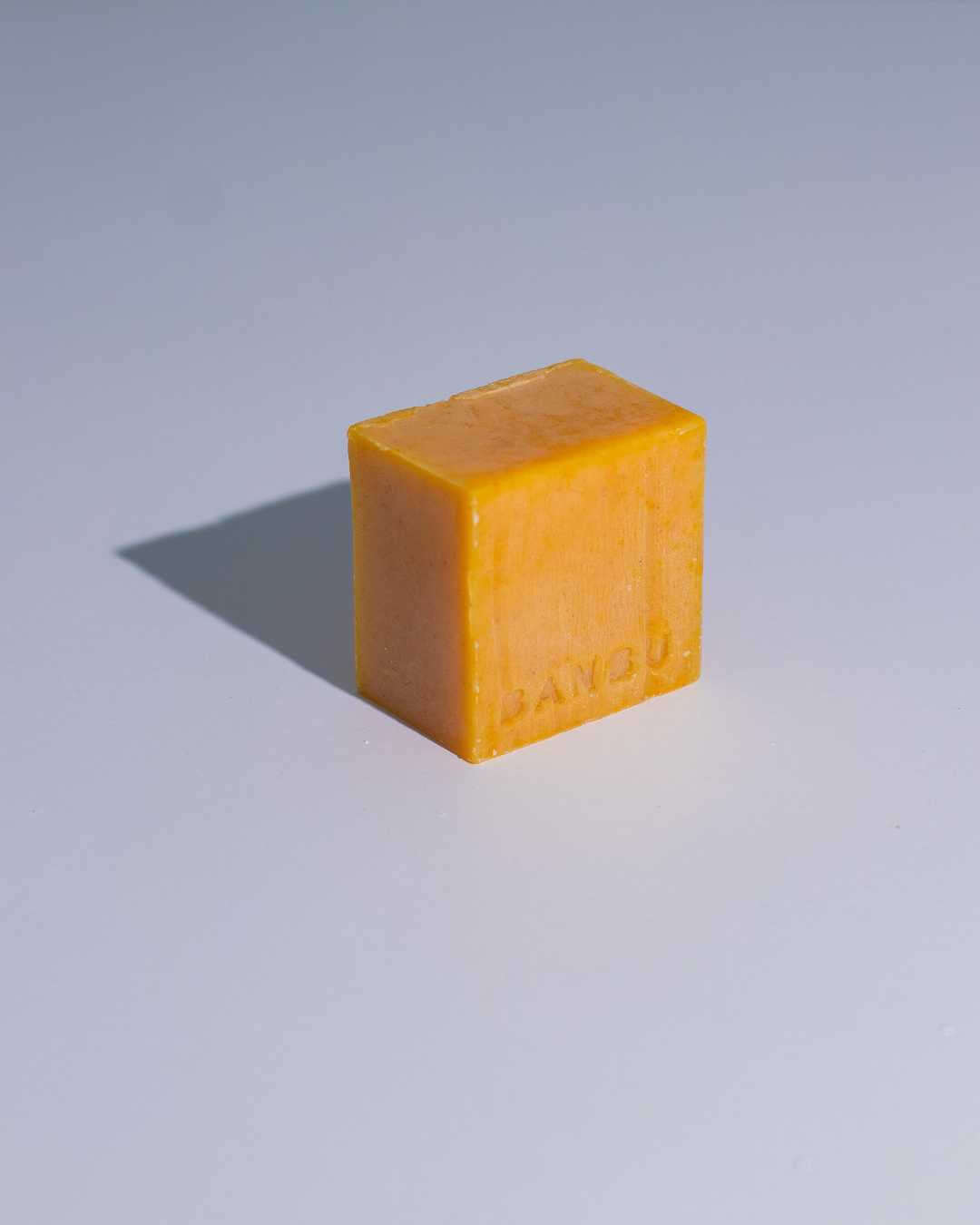 Jabón de ducha sólido Banbu, color naranja cítrico y forma rectangular, sobre fondo blanco neutro.