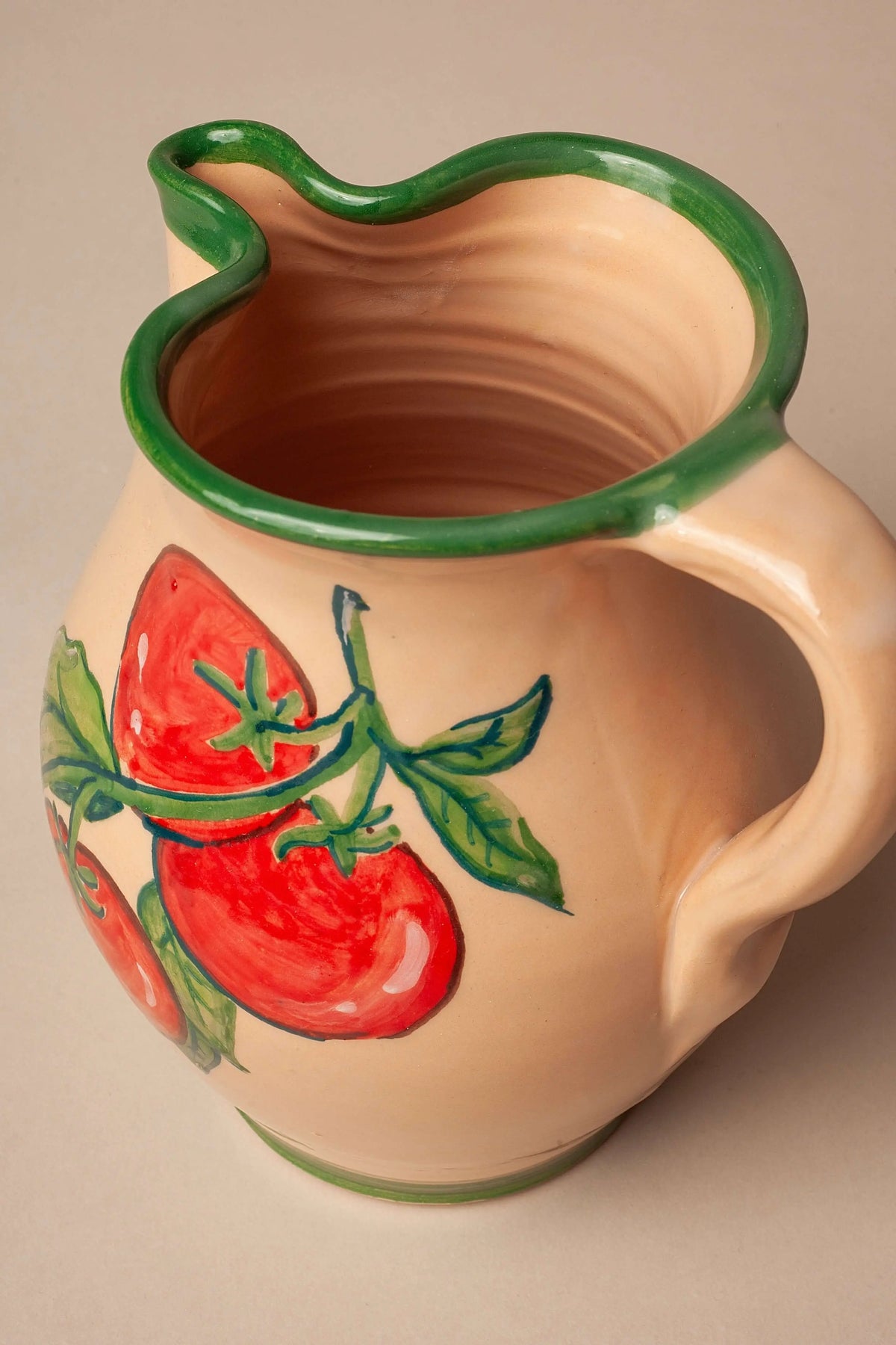 Jarra de cerámica artesanal color crema con borde verde y dibujo pintado a mano de tomates rojos con hojas verdes.
