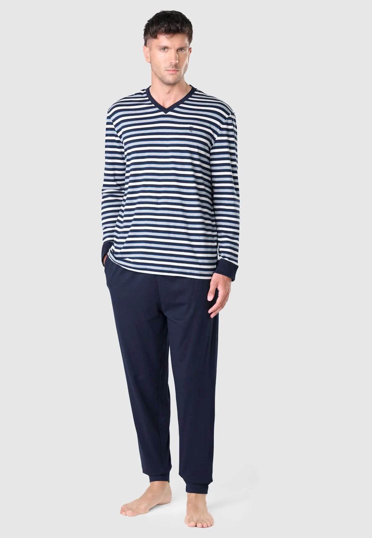 Modelo con pijama de hombre: camiseta cuello pico a rayas azules/grises y pantalón largo liso azul marino de algodón.