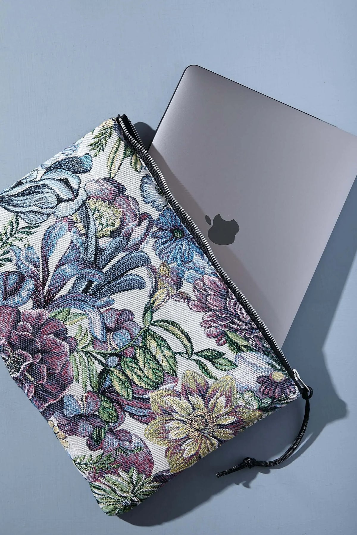 Funda de ordenador en tejido jacquard con estampado de flores en tonos azules, morados y verdes sobre fondo claro.