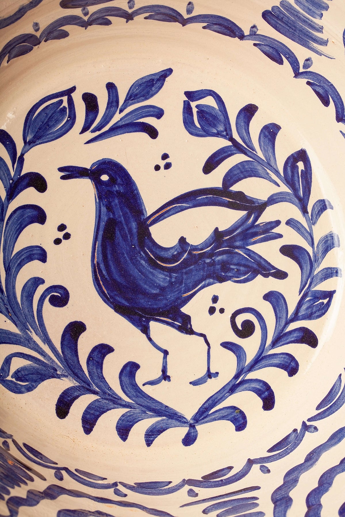 Hand-painted ceramic bowl with a blue bird motif surrounded by a floral wreath on a cream background.