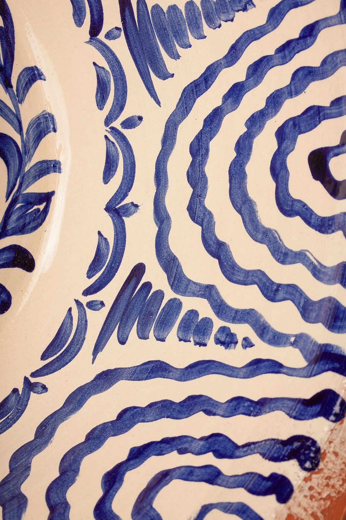 Handcrafted ceramic bowl with intricate hand-painted blue wavy lines and leaf patterns on a cream background.