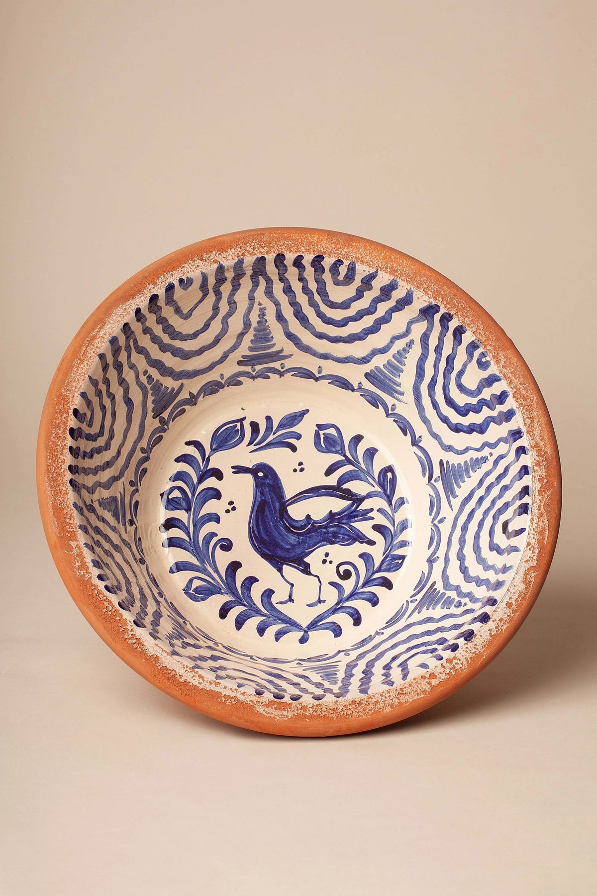 Lebrillo de cerámica artesanal con motivos de aves y ondas pintadas en azul sobre fondo blanco y borde de barro natural.