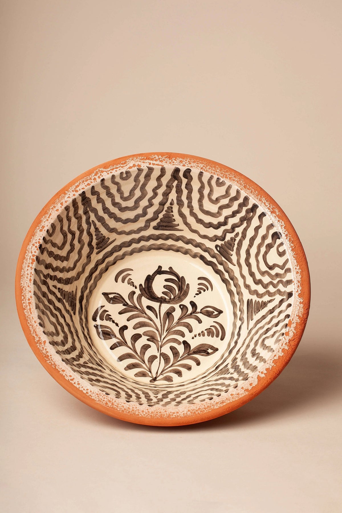 Lebrillo de cerámica artesanal con motivos florales y geométricos en negro sobre fondo crema y borde de barro natural.
