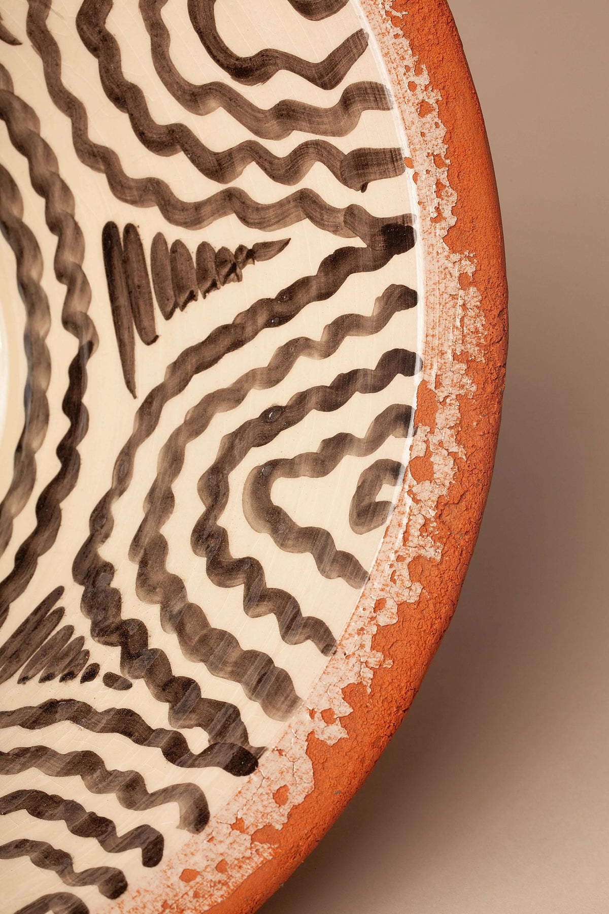Lebrillo de cerámica con borde en terracota y decorado interior con motivos ondulados en negro sobre fondo crema.
