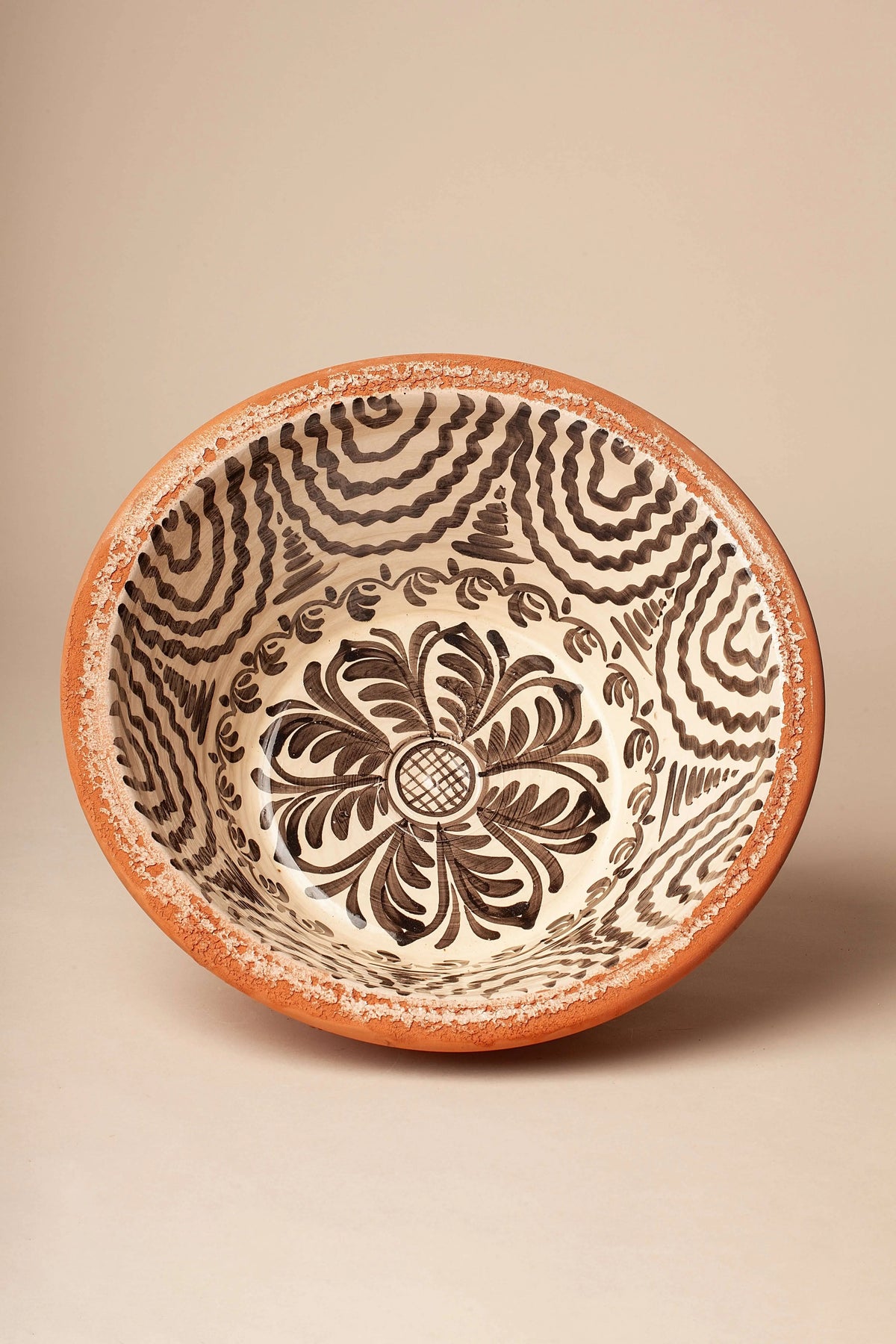 Lebrillo de cerámica con borde de barro natural y centro decorado con motivos florales y geométricos en negro sobre crema.