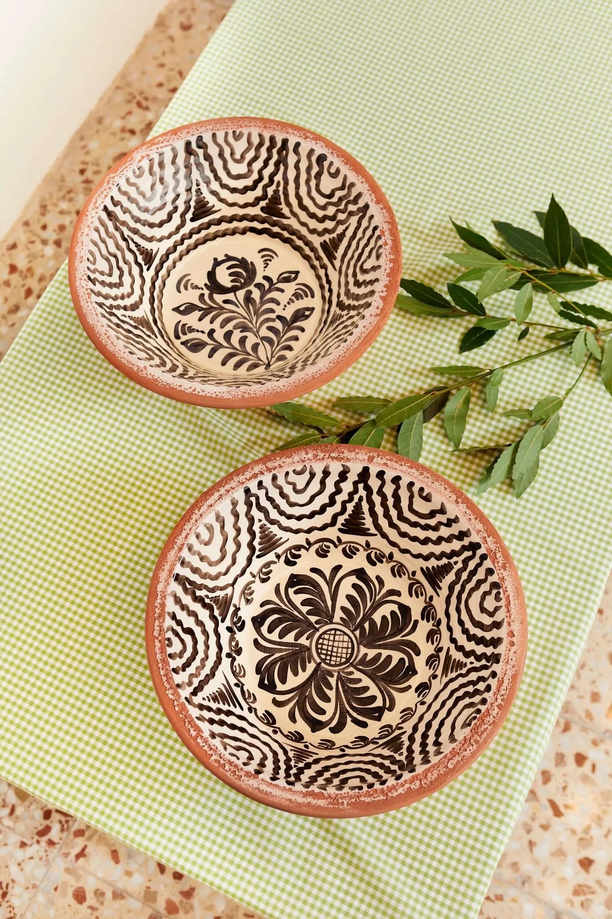 Dos lebrillos de cerámica artesanal con motivos florales y geométricos pintados en negro sobre fondo crema y borde rojo.