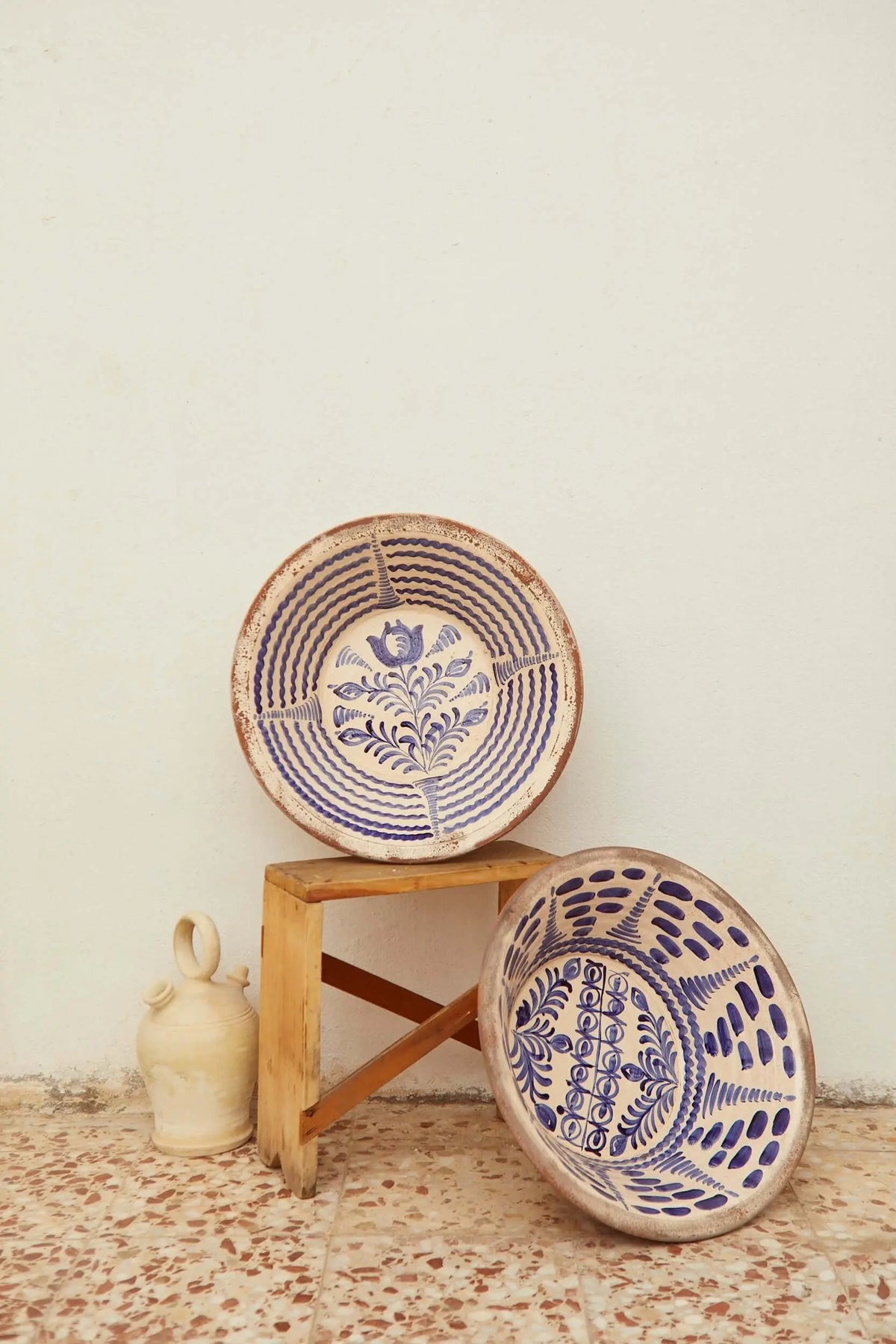 Two traditional Granada ceramic bowls with hand-painted blue floral patterns on a rustic wooden stool.