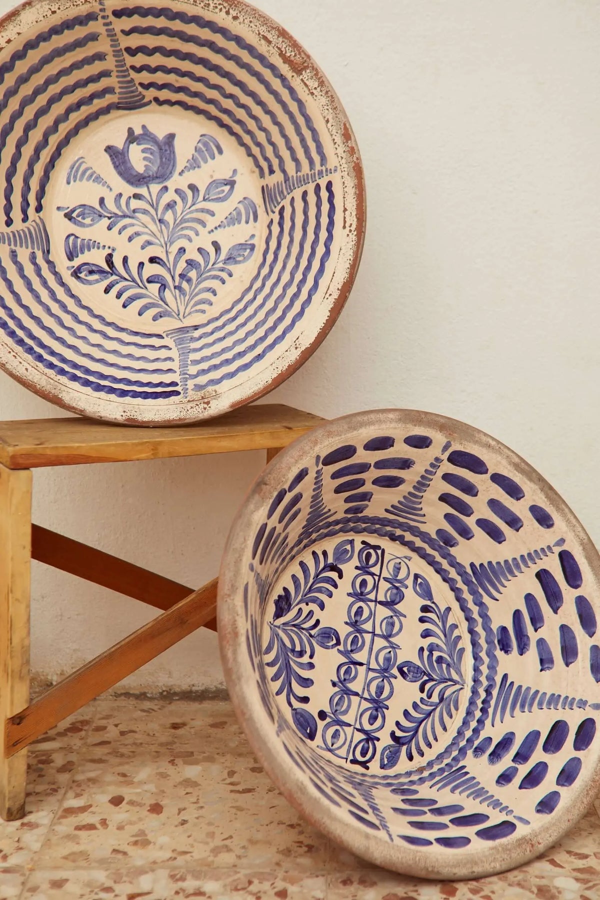 Dos lebrillos de cerámica granadina con decoración floral en azul sobre fondo crema, apoyados en un taburete de madera.