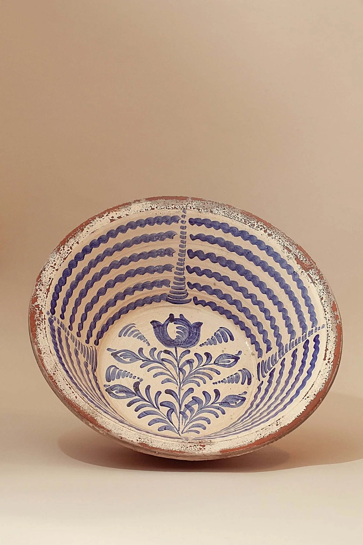 Lebrillo de cerámica artesanal con motivos florales y líneas onduladas en color azul sobre fondo crema.
