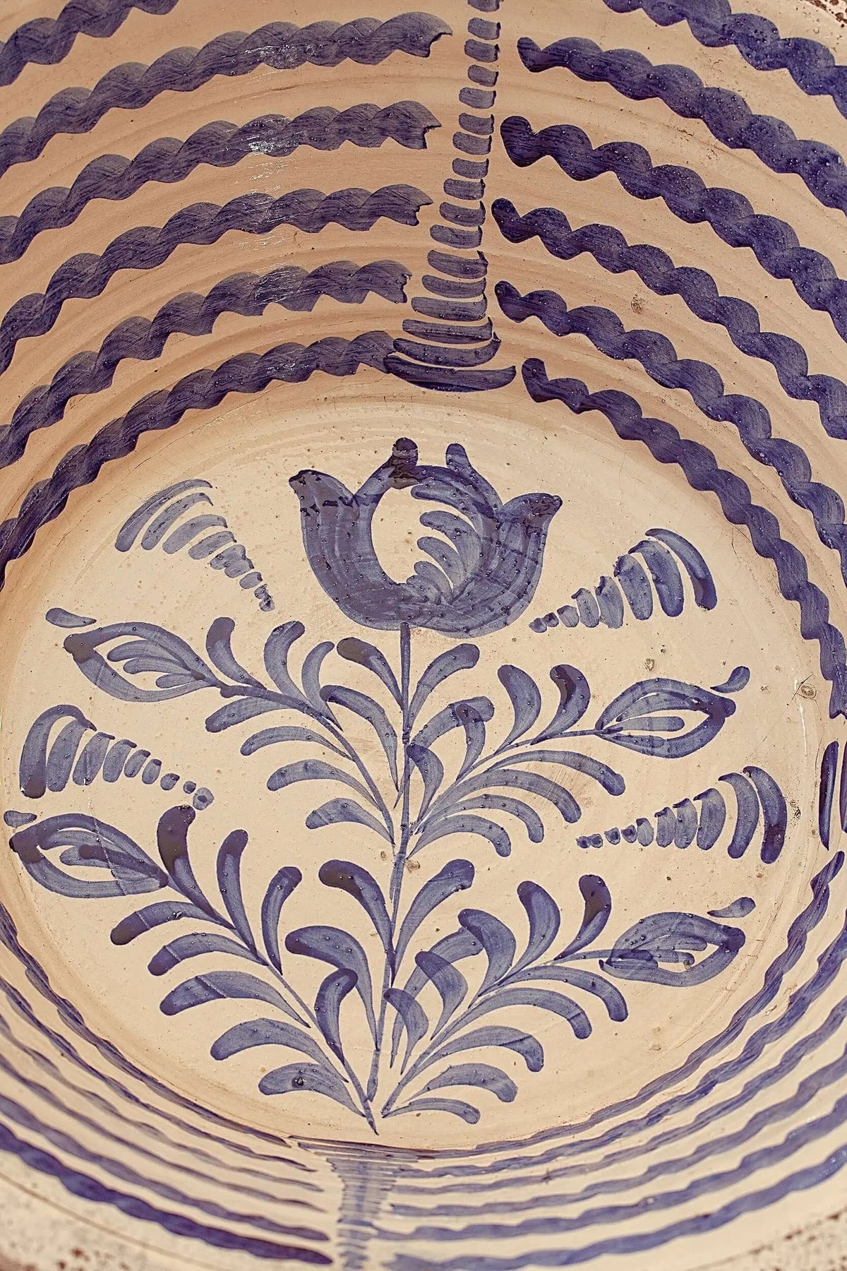 Lebrillo de cerámica artesanal con fondo crema y pintura azul tradicional de motivos florales y líneas onduladas.