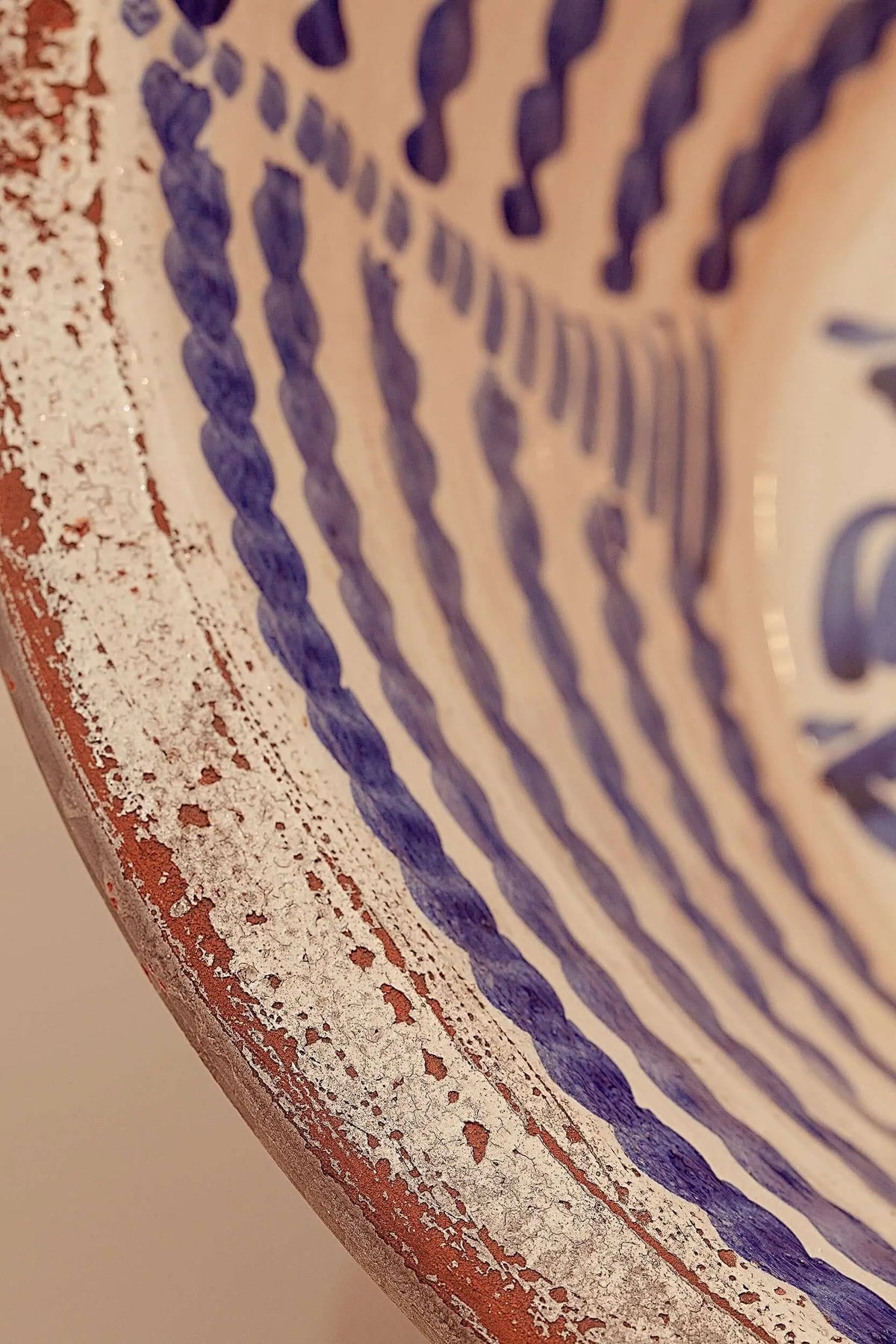 Lebrillo de cerámica artesanal con motivos lineales azules sobre fondo blanco y borde de barro natural visto.