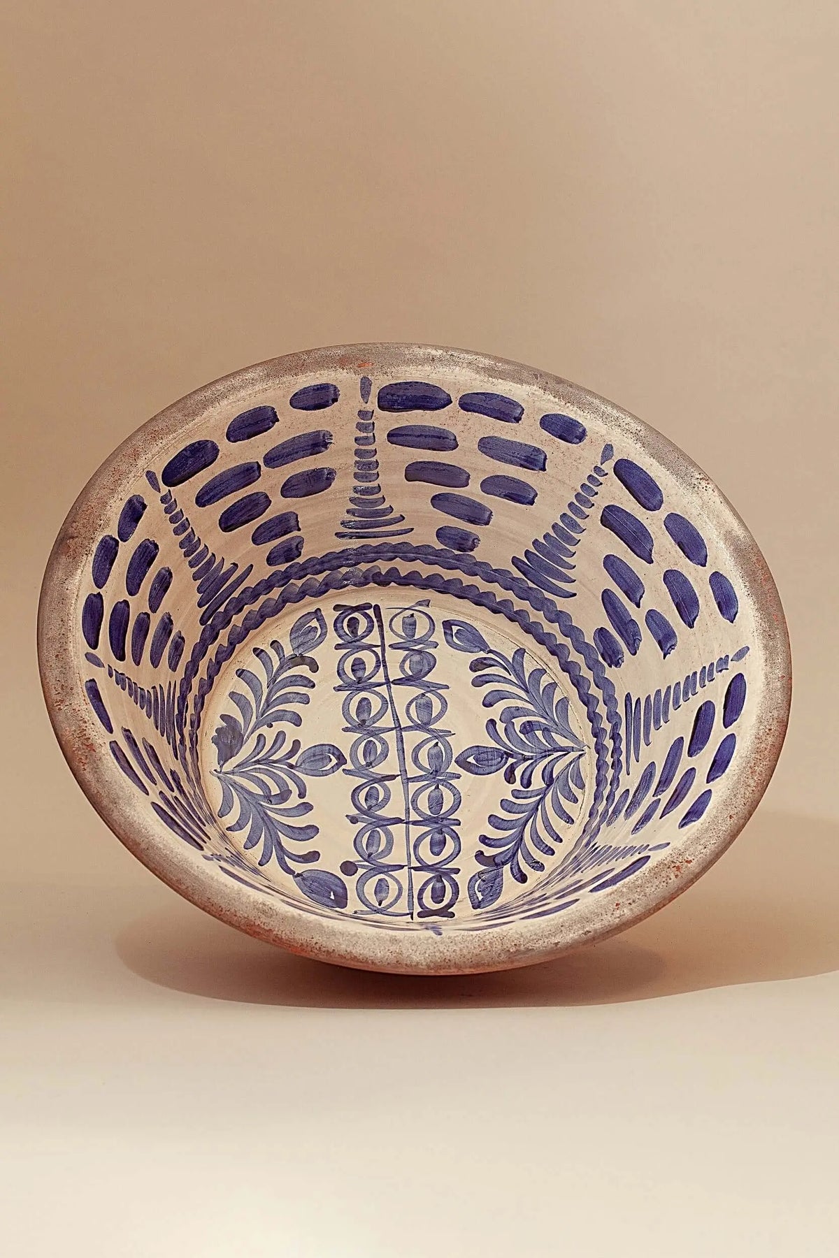Hand-painted ceramic bowl with traditional blue floral and dashed patterns on a rustic, off-white background.