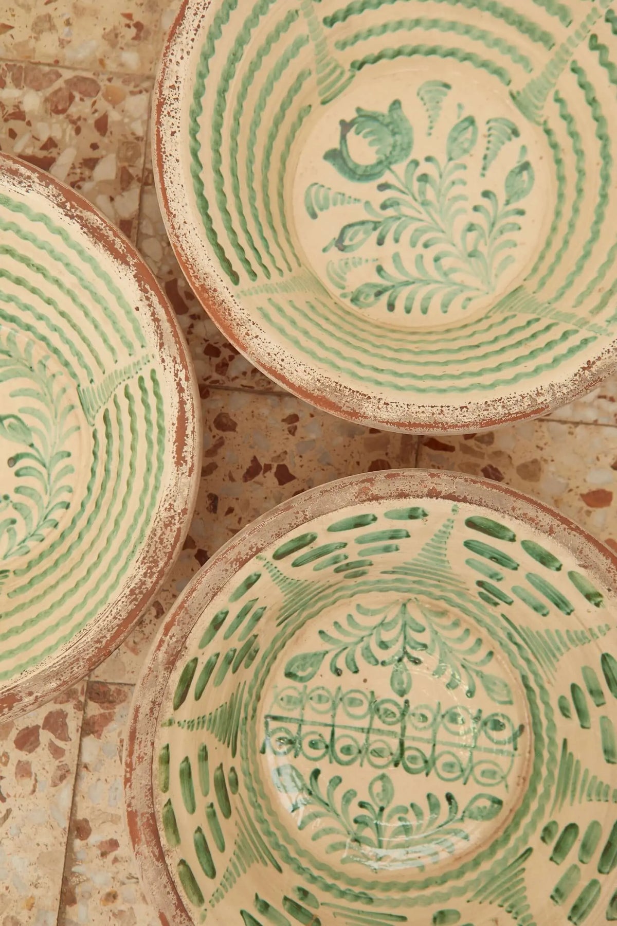 Tres lebrillos de cerámica artesanal con motivos vegetales verdes sobre fondo crema y acabado rústico de barro visto.