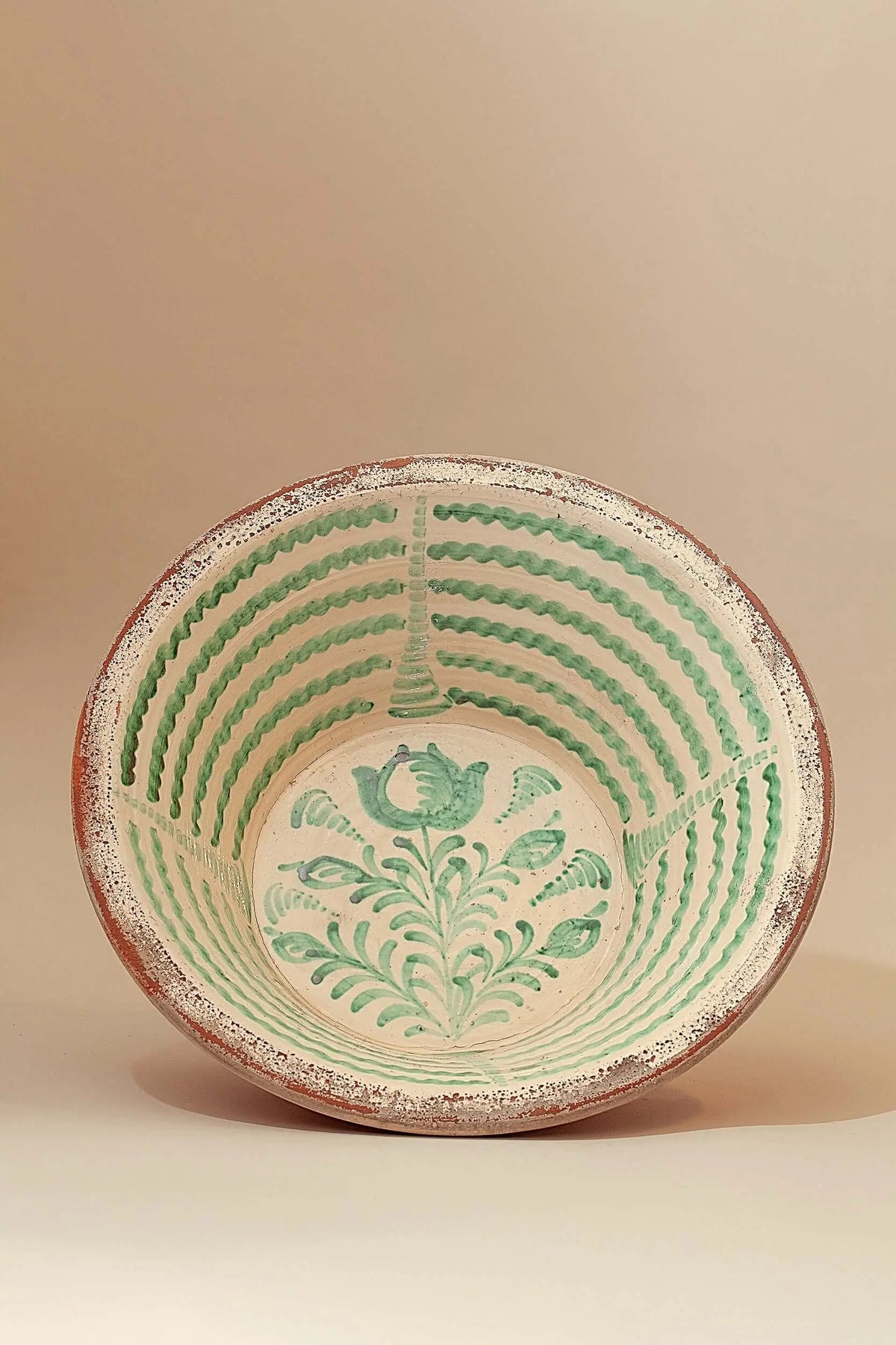 Lebrillo de cerámica artesanal con motivos florales y líneas onduladas pintadas en color verde sobre fondo crema.