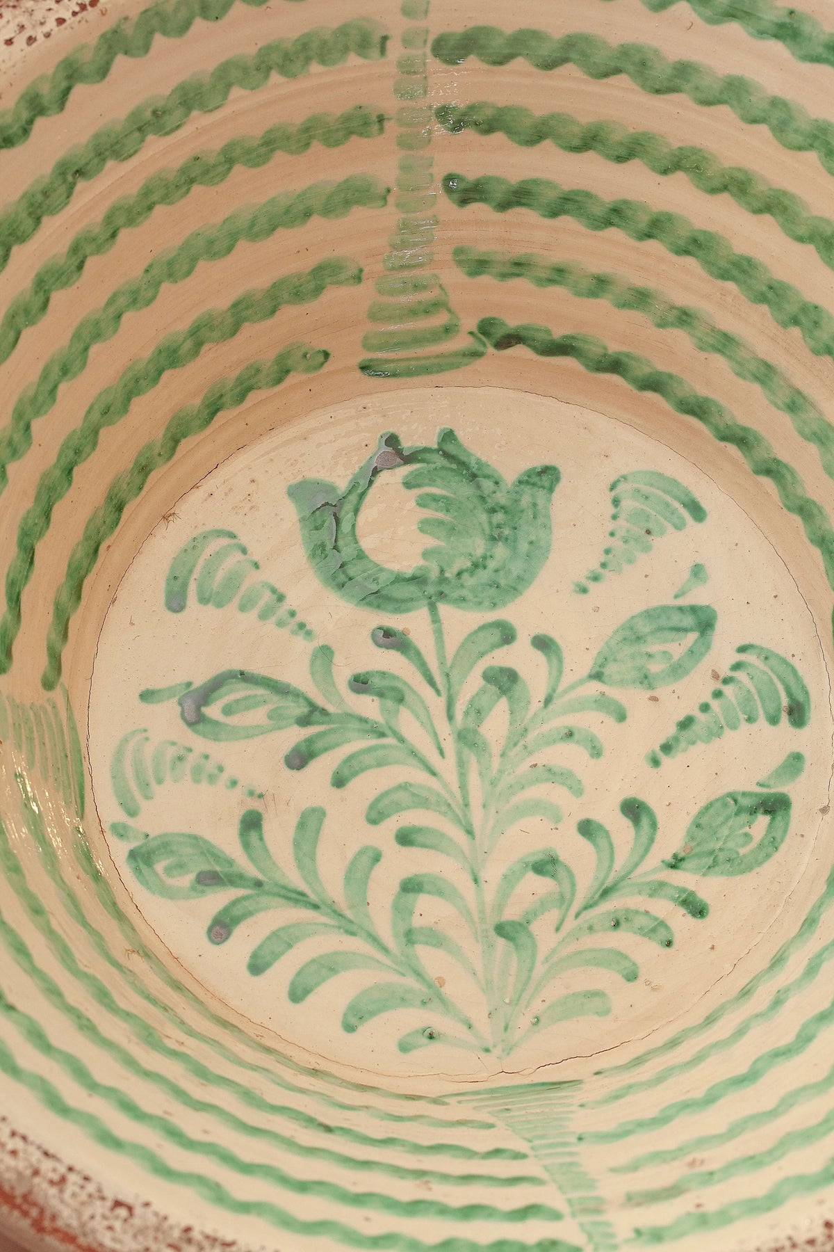Lebrillo de cerámica artesanal con fondo crema y pintura verde de estilo tradicional con motivos florales y geométricos.