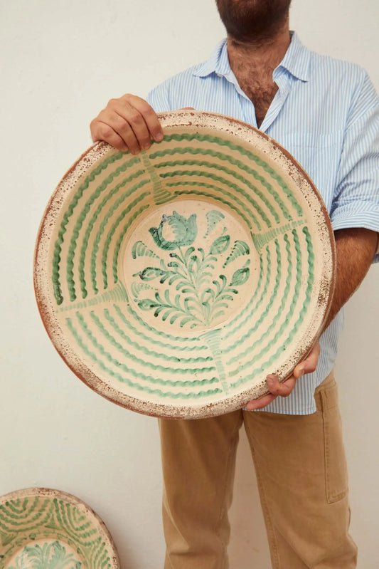 Handcrafted ceramic bowl with green wavy lines and floral center design on a rustic, cream-colored terracotta base.