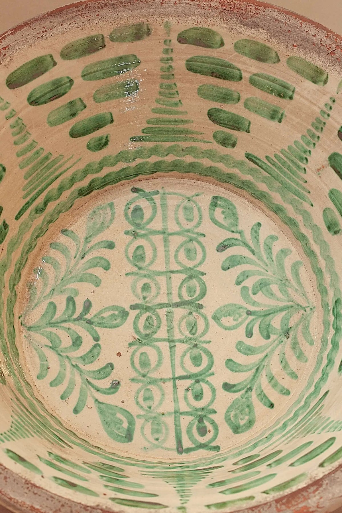 Lebrillo de cerámica artesanal con decoración de motivos vegetales y geométricos pintados en color verde sobre fondo crema.