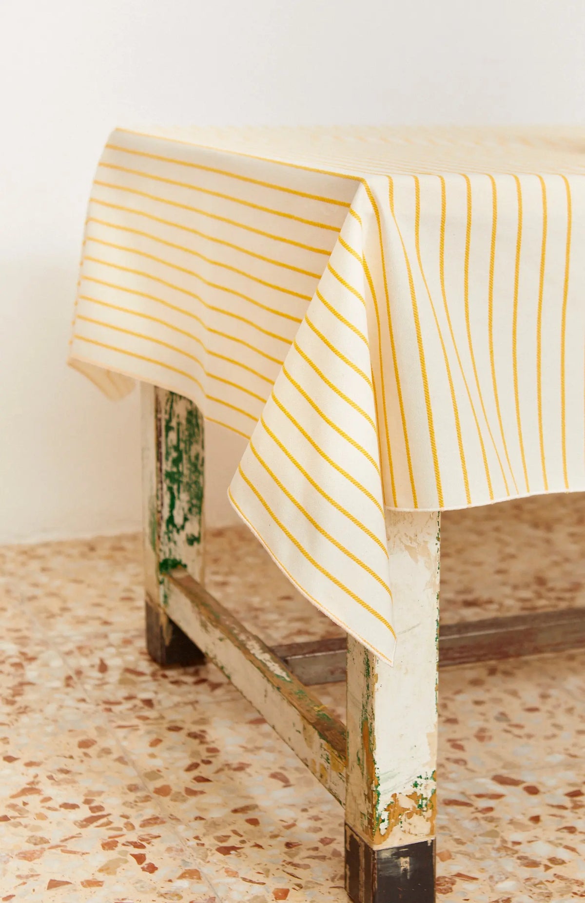 Mantel de tela color crema con finas rayas verticales amarillas, extendido sobre una mesa de madera desgastada.