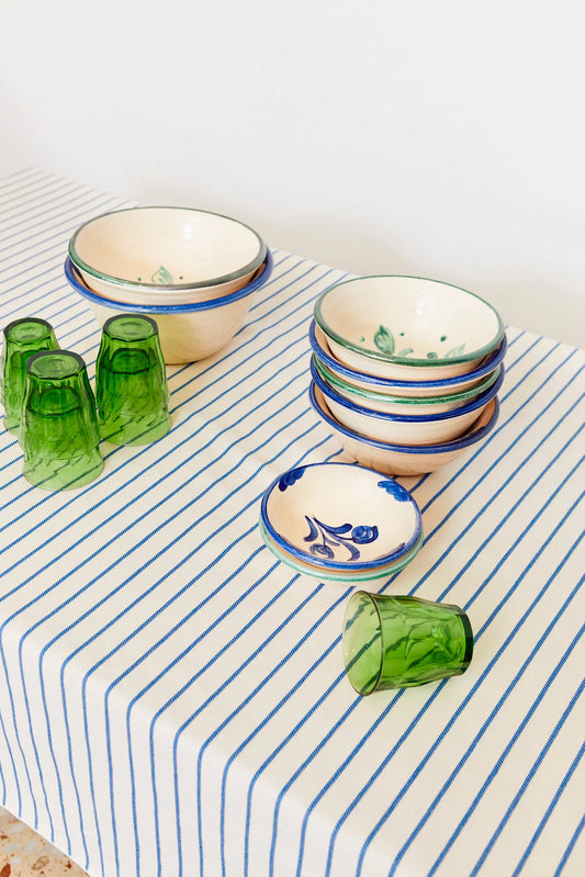 Mantel de tela blanco con finas rayas azules, sobre el que se disponen cuencos de cerámica y vasos de vidrio verde.