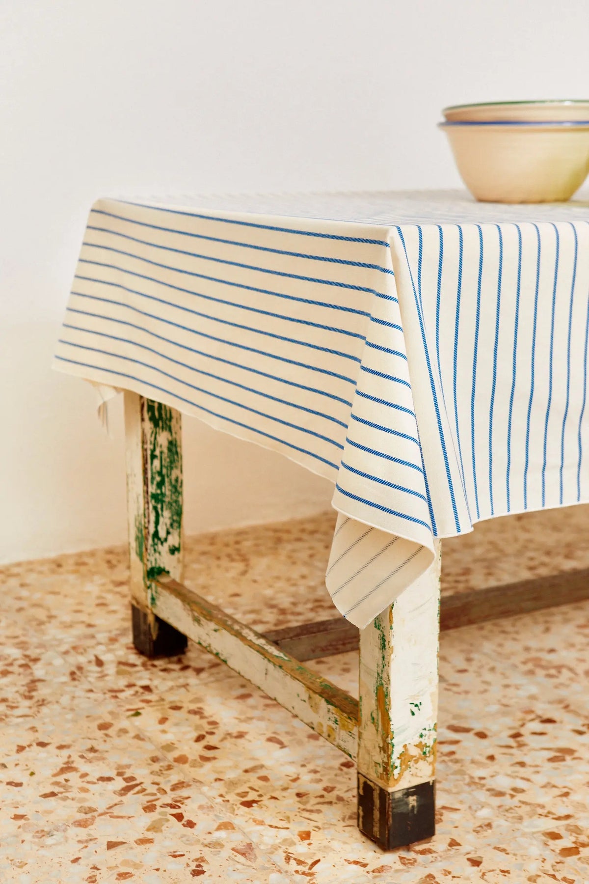 Off-white tablecloth with thin blue vertical chain-link stripes covering a rustic wooden table.