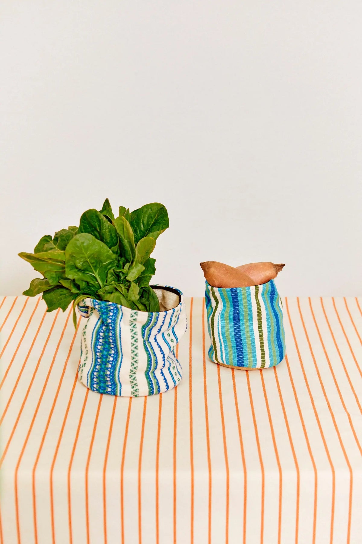Tablecloth with thin orange stripes on white fabric, featuring two matching blue-patterned fabric storage baskets.