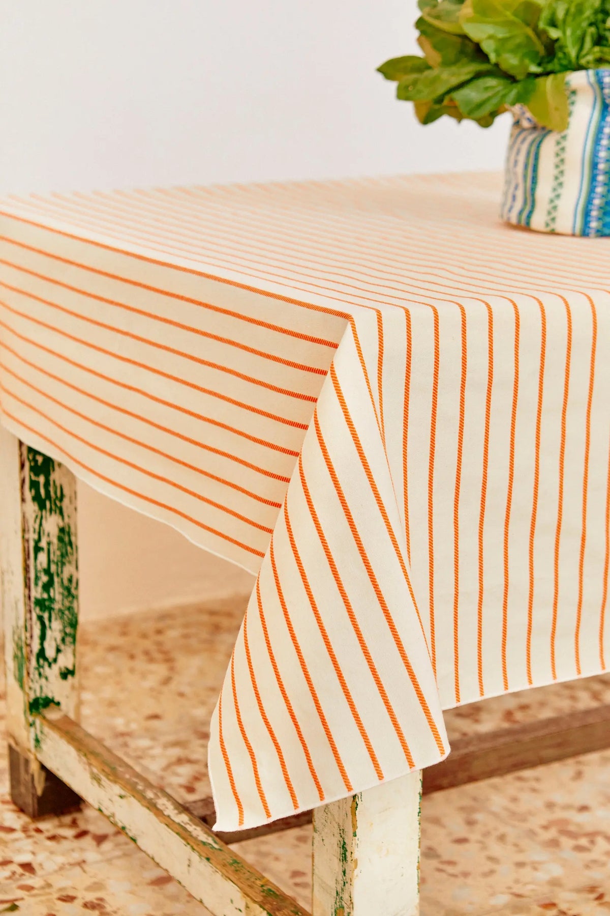 Mantel de algodón blanco con rayas verticales finas en color naranja sobre una mesa de madera rústica desgastada.