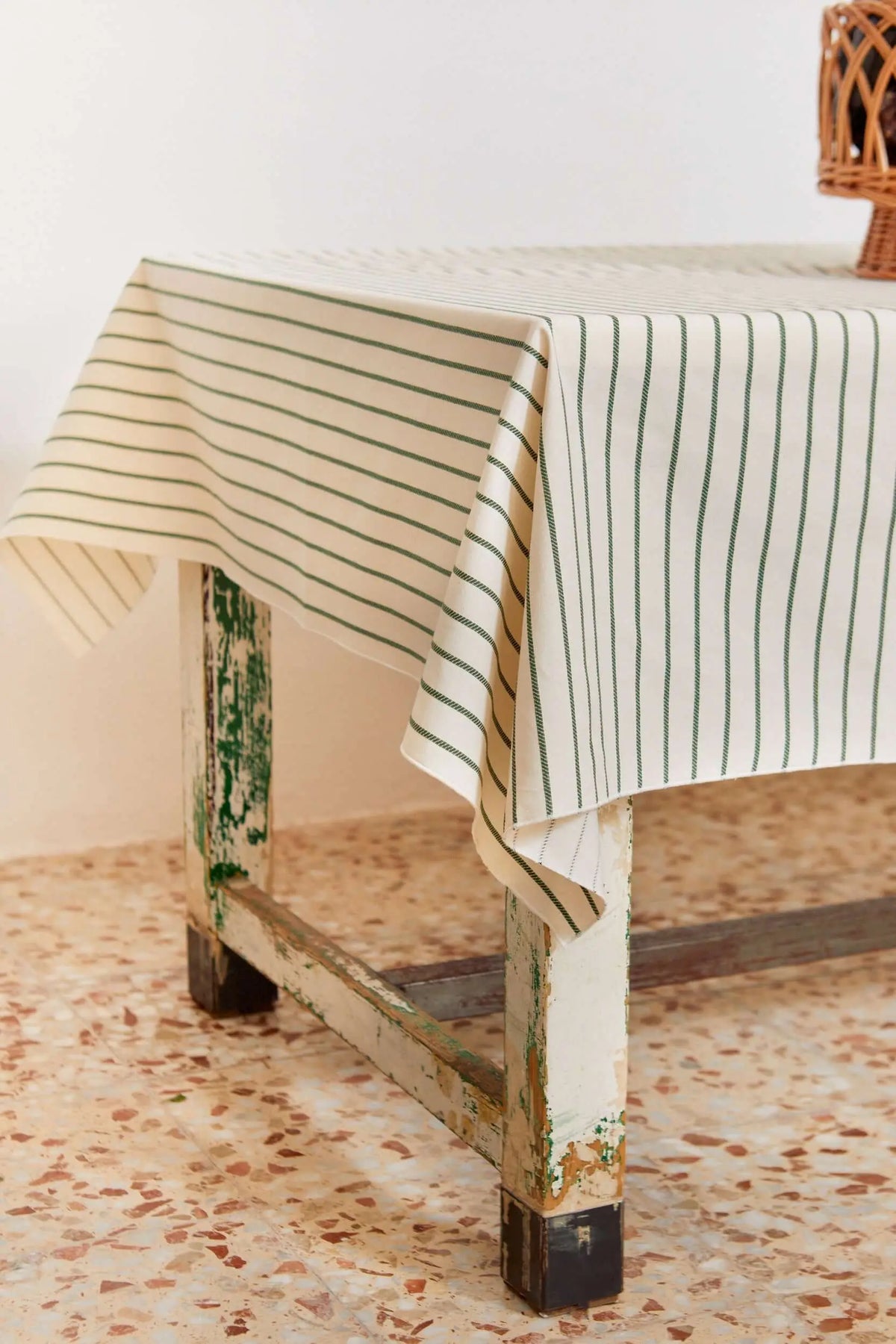 Off-white tablecloth with thin, vertical green chain-link stripes, draping over a rustic, distressed wooden table.